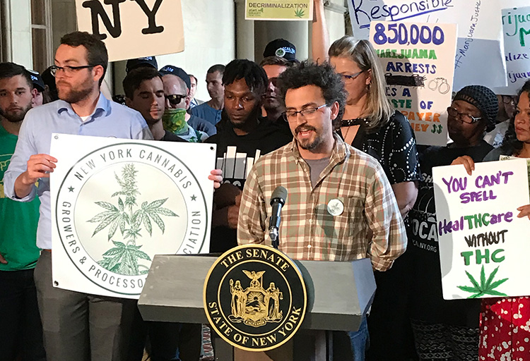 CANY President Allan Gandelman speaking at the NY Senate on behalf of the NYCGPA. Behind him are cannabis activists holding signs about the NYCGPA, THC in Healthcare and marijuana decriminalization.