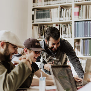a group of men laughing at a computer screen at work