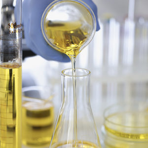 A gloved hand pouring yellow liquid into a measuring glass