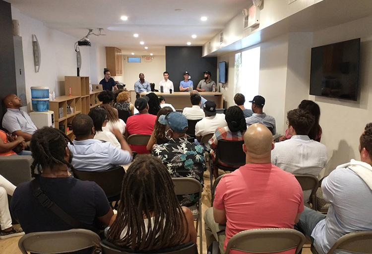 A cannabis industry meeting in a small room with a panel of five men at the front and several audience members seated.